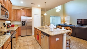 A kitchen with granite countertops, stainless steel appliances, wooden cabinets, a dishwasher, and a built-in island with a sink. - Paradise Palms 2956 (Kissimmee)