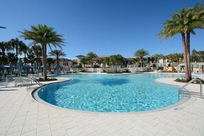 Une piscine bordée de palmiers, avec des chaises longues et un bâtiment en arrière-plan.