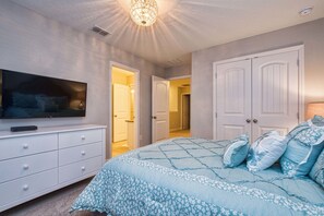 Quarto com uma cama grande, uma televisão em uma cômoda e duas portas que dão para outros ambientes.