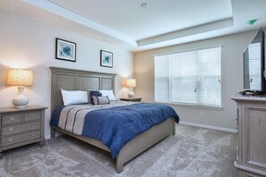 A bedroom with a bed, two bedside tables with lamps, a dresser, and a window with blinds. - Solara Resort 9021 (Kissimmee)