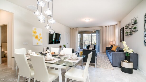 Una sala de estar moderna con una mesa de comedor de vidrio, sillas blancas, un sofá y un televisor montado en la pared.