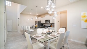 Een moderne keuken met witte kastjes, roestvrijstalen apparatuur en een eethoek met een glazen tafel en witte stoelen.