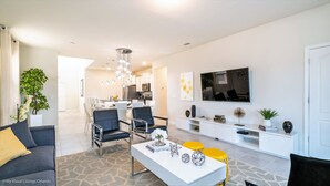Een moderne woonkamer met een bank, salontafel en stoelen. Er is een eethoek met een tafel en stoelen. In de achtergrond is een keuken zichtbaar.