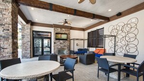A covered patio area with round tables and chairs, a stone fireplace, and a television mounted on the wall. - Solterra 5500 (Davenport)
