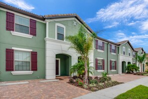 A row of townhouses with green facades, red shutters, and a brick pathway leading to the entrance. - Solterra 4663 (Davenport)