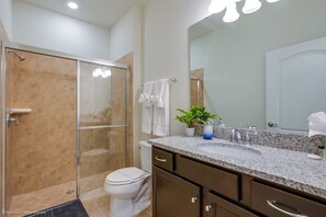 A modern bathroom with a glass shower enclosure, a toilet, a sink with a granite countertop, and a mirror above the sink. - Solterra 4663 (Davenport)