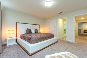Une chambre à coucher avec un grand lit, des tables de chevet blanches et un sol recouvert d’une moquette.