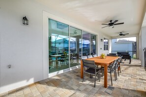 Une terrasse avec une table et des chaises en bois, une porte vitrée donnant sur une pièce et des ventilateurs de plafond.