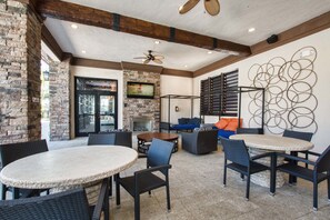Un patio abrité avec des tables et des chaises rondes, une cheminée en pierre et un téléviseur fixé au mur.
