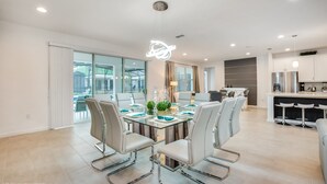A modern dining area with a glass table, white chairs, and a unique ceiling light fixture.