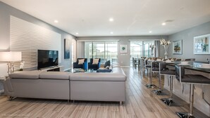 A spacious living area with a large sectional sofa, a flat-screen TV, and a dining area with high chairs and a table. - Sonoma Resort 2619 (Kissimmee)