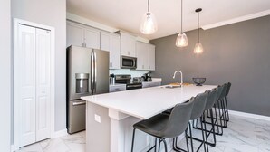 A modern kitchen with white cabinets, stainless steel appliances, and a central island with bar stools. - Storey Lake 4958 (Kissimmee)