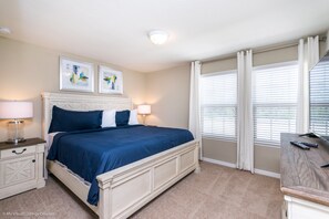Une chambre à coucher comprenant un lit, des tables de chevet, un bureau et une fenêtre avec des stores.