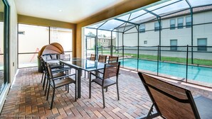A patio with a glass table and chairs, a brick floor, and a view of a swimming pool and houses. - Windsor at Westside 1852 (Kissimmee)