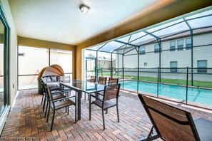 Une terrasse avec une table et des chaises en verre, un sol en briques et une vue sur une piscine et des maisons.