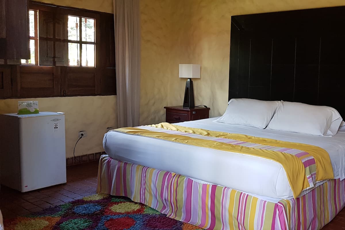 Habitación de hotel con cama, mesita de noche, escritorio, silla, ventana y refrigerador.