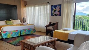 Habitación de hotel con cama, sofá, una mesita y balcón con vistas a zonas verdes.