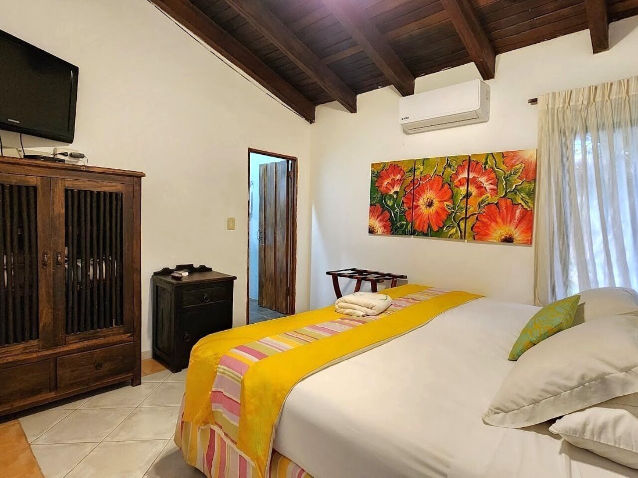 A bedroom with a bed, a wooden cabinet, a television, and a painting.