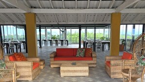Un salón al aire libre con mobiliario de mimbre, piso a cuadros y ventanas amplias.