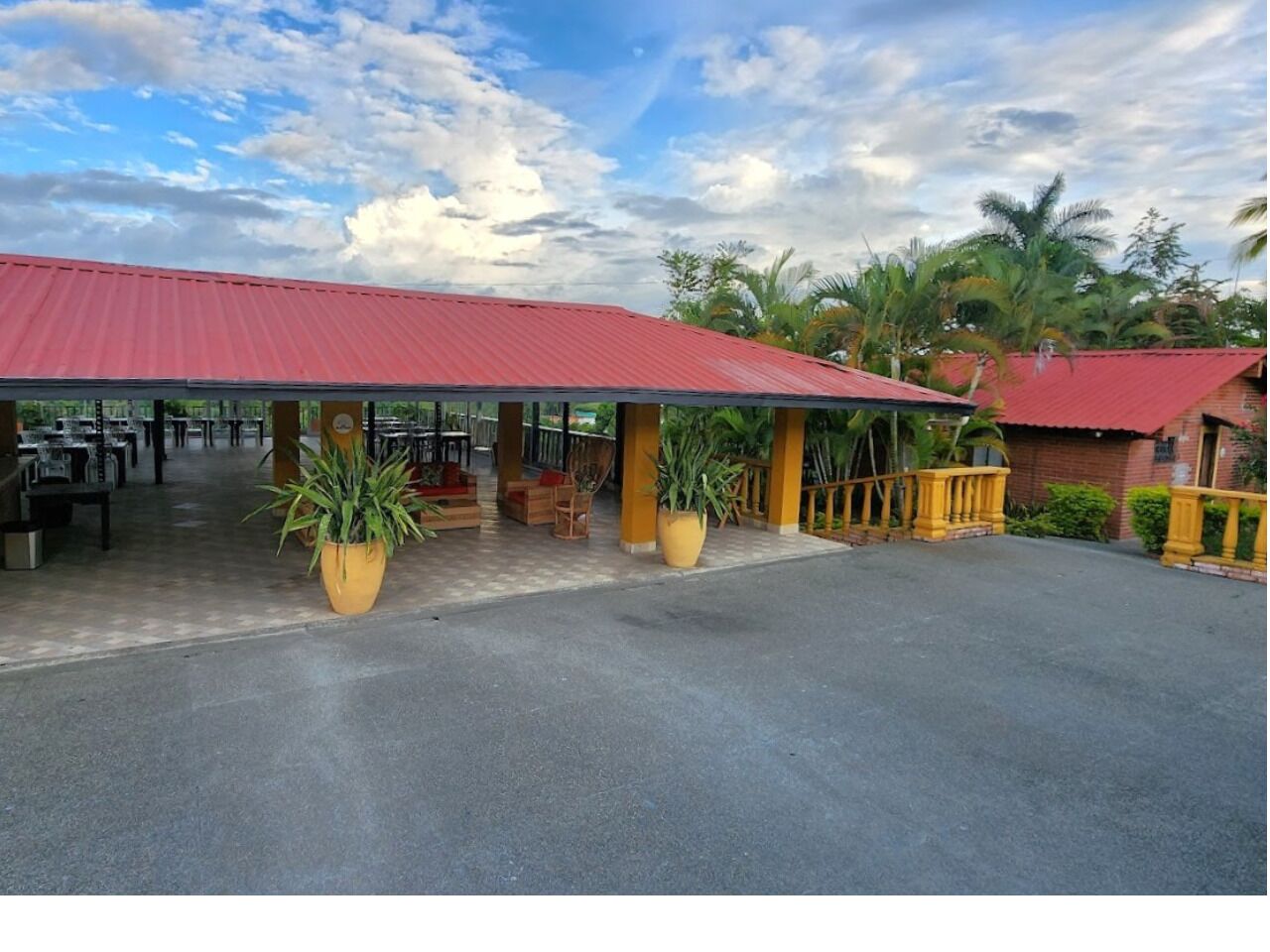 A covered outdoor seating area with tables and chairs, potted plants, and a red roof.