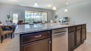 Eine geräumige Küche mit Granit-Arbeitsplatten, Edelstahlgeräten und Pendelleuchten.