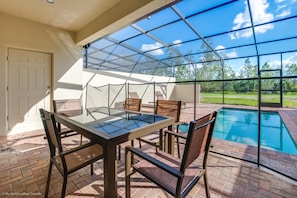 Ein durch Glas geschützter Patio mit Pool, Tisch und Stühlen sowie einer Tür.