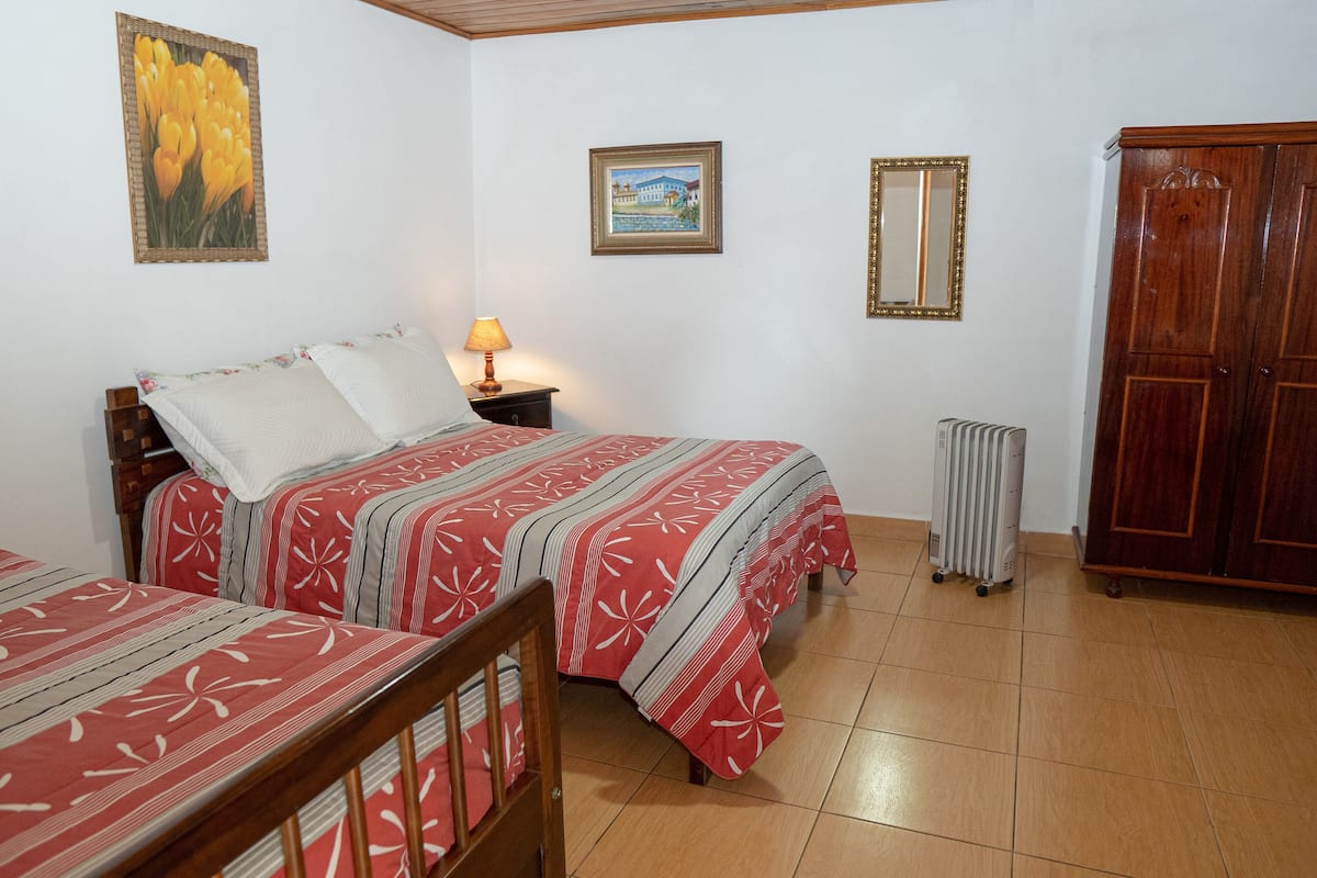 A bedroom with two beds, a nightstand, a lamp, a radiator, and a wardrobe.