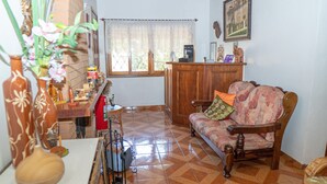 Una sala de estar con un sofá de madera, una mesa de comedor con un florero y una ventana con cortina de encaje.