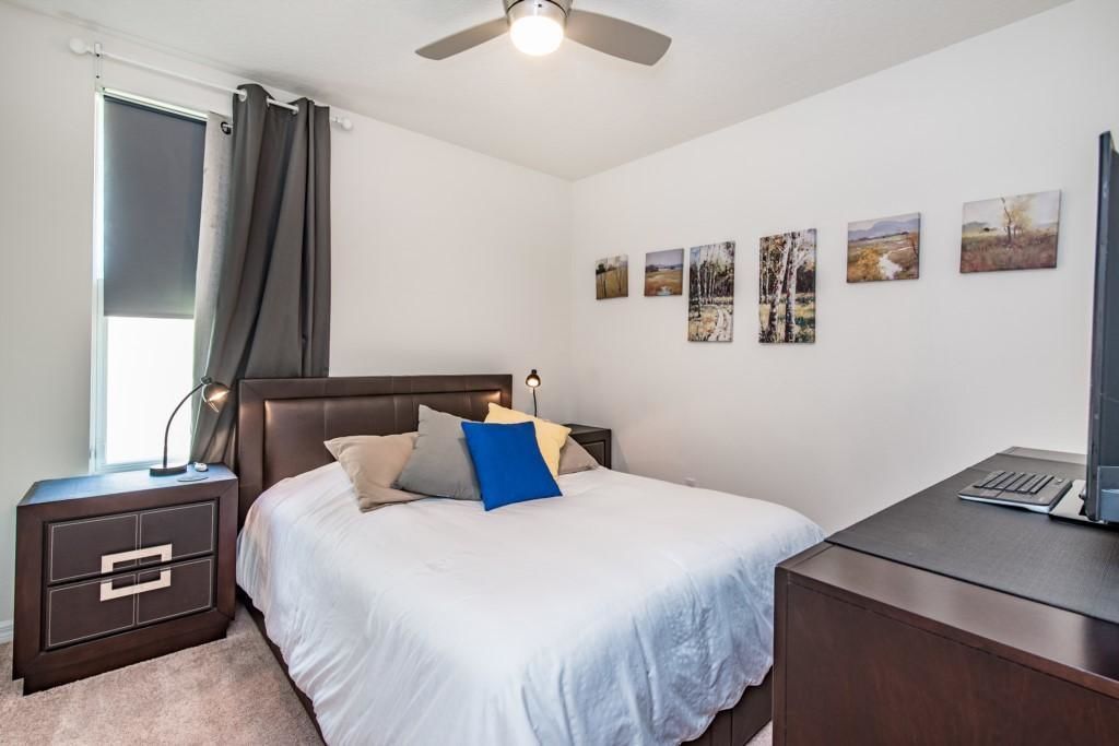 A bedroom with a bed, a desk, a nightstand, a ceiling fan, and wall art.