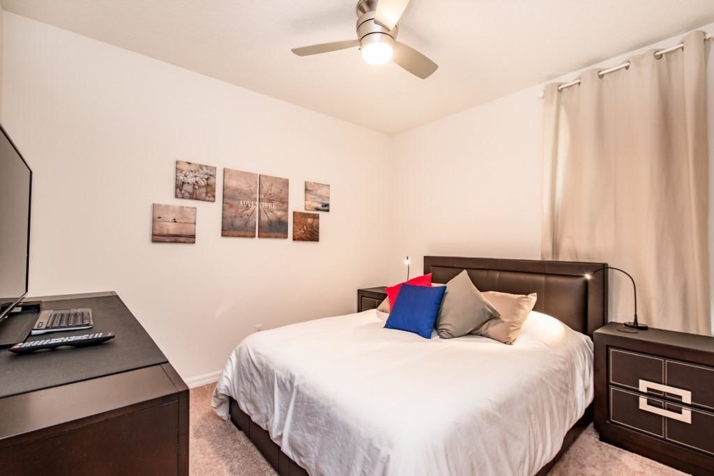 A bedroom with a bed, a desk, and a ceiling fan.
