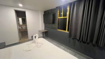 A modern hotel room with a large bed, a small bedside table, a mirror, and a window with curtains.