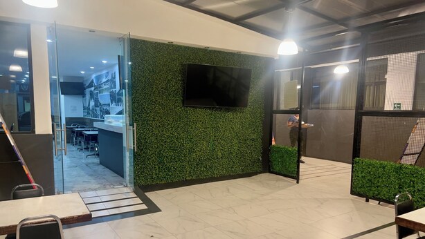 Ein moderner Arbeitsraum mit einer grünen Wand, einem Flachbildfernseher und einer Sitzecke mit Tischen und Stühlen.