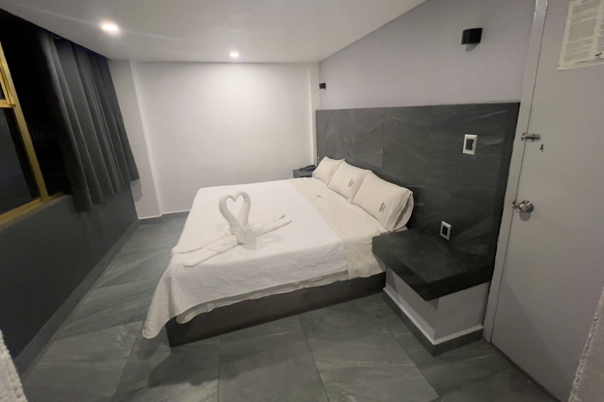 Ein Hotelzimmer mit Bett, Nachttisch, Kopfteil und einer Tür.