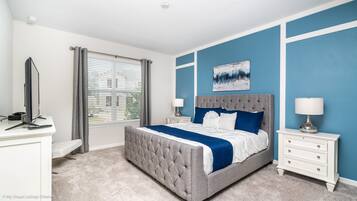 A bedroom with a large bed, a desk, a chair, a lamp, and a window with blinds.