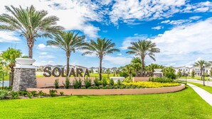 A well-maintained lawn with a sign reading "SOLARA" surrounded by palm trees and a clear blue sky. - Windsor at Westside 1749 (Kissimmee)