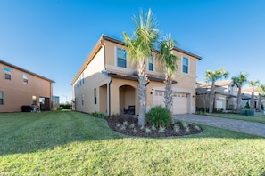 A two-story house with a front porch, palm trees, and a well-maintained lawn.