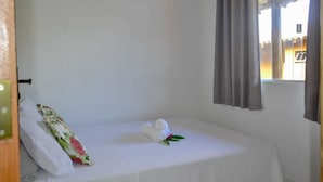 A single bed with white bedding, a floral pillow, and a rolled towel with a green leaf. - Villa Nobre Residence (Porto Seguro)