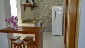 A kitchen with a white refrigerator, a wooden countertop, a sink, and a shelf with kitchen items. - Villa Nobre Residence (Porto Seguro)