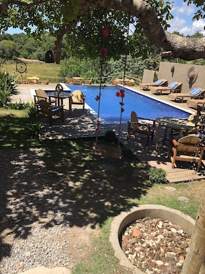 A backyard with a swimming pool, lounge chairs, and a deck area.