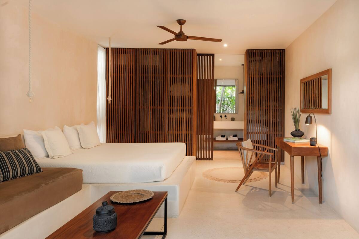 A modern bedroom with a bed, a wooden desk, a chair, and a small table.