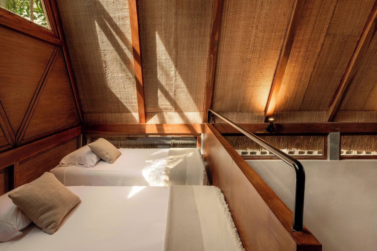 A room with a wooden ceiling and a window, two beds with pillows, and a metal handrail.