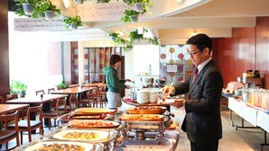 A buffet setup with various food items and a person serving. - Hotel New Carina (Morioka)
