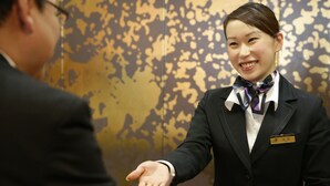 A hotel reception area with a wooden reception desk and a patterned wall in the background. - Hotel New Carina (Morioka)