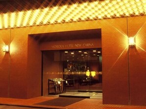 The exterior of Morooka Hotel New Carina with a modern design, featuring a glass entrance and illuminated signage.