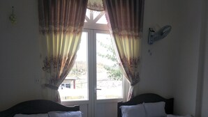 A room with two beds, a window with curtains, a wall-mounted fan, and a view of the outside. - Hotel Nguyen Ngoc (Cu Jut)