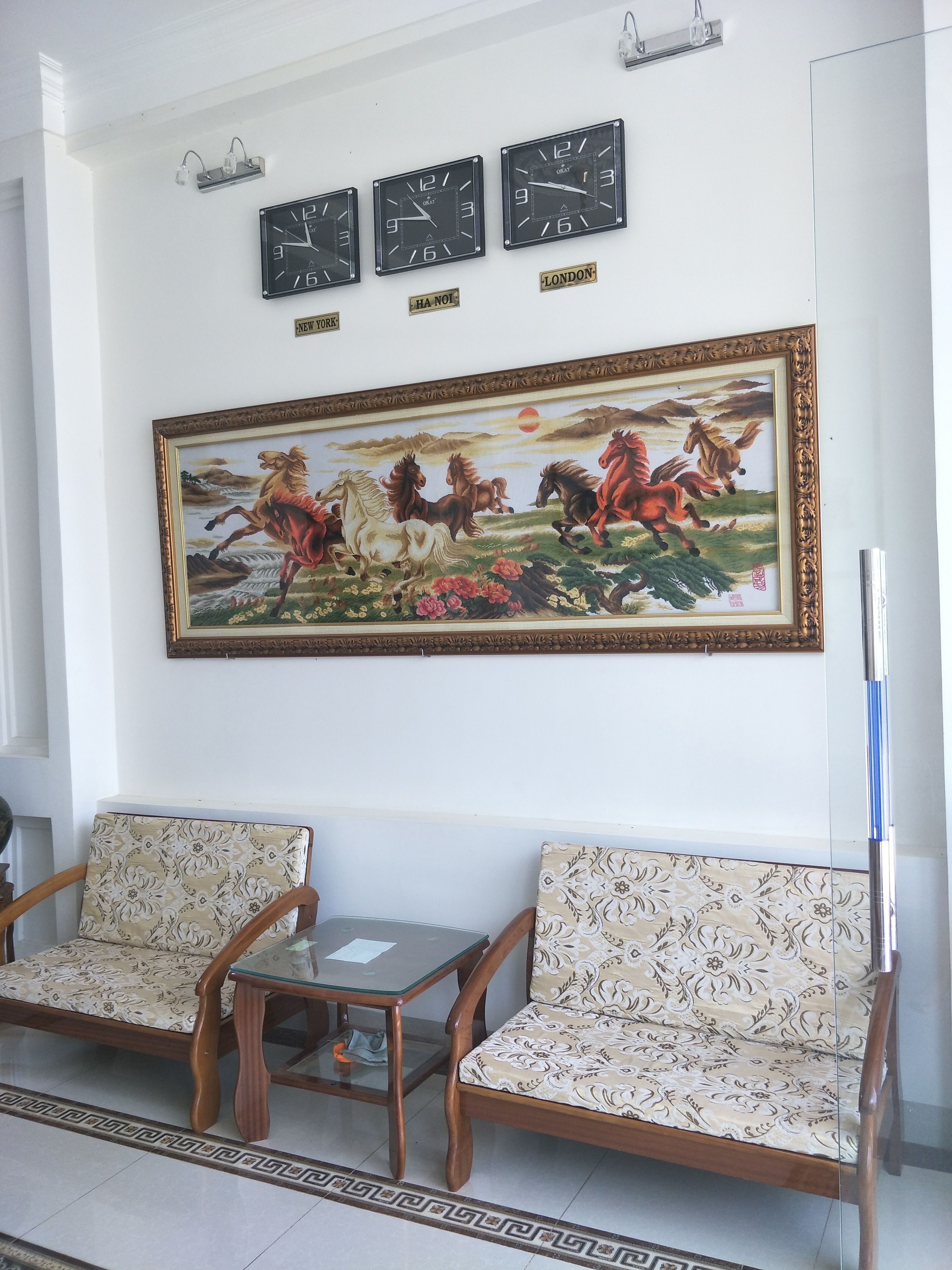 Uma sala de espera com duas cadeiras de madeira, uma mesa de vidro e um quadro grande com cavalos.