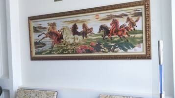 Uma sala de espera com duas cadeiras de madeira, uma mesa de vidro e um quadro grande com cavalos.