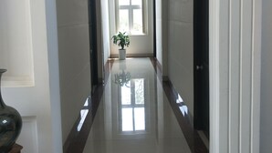 A hallway with a glossy tiled floor, white walls, and a potted plant at the end. - Hotel Nguyen Ngoc (Cu Jut)