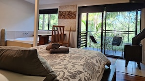 A bedroom with a large bed, a wooden chair, a desk, and a view of greenery through a sliding door. - Alaya Ascend  |  Seminyak Pool-view Room |  Sunshine Coast Retreat (Eudlo)