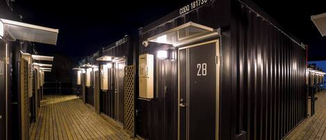 Una hilera de habitaciones de hotel oscuras, numeradas, con una terraza de madera al frente.